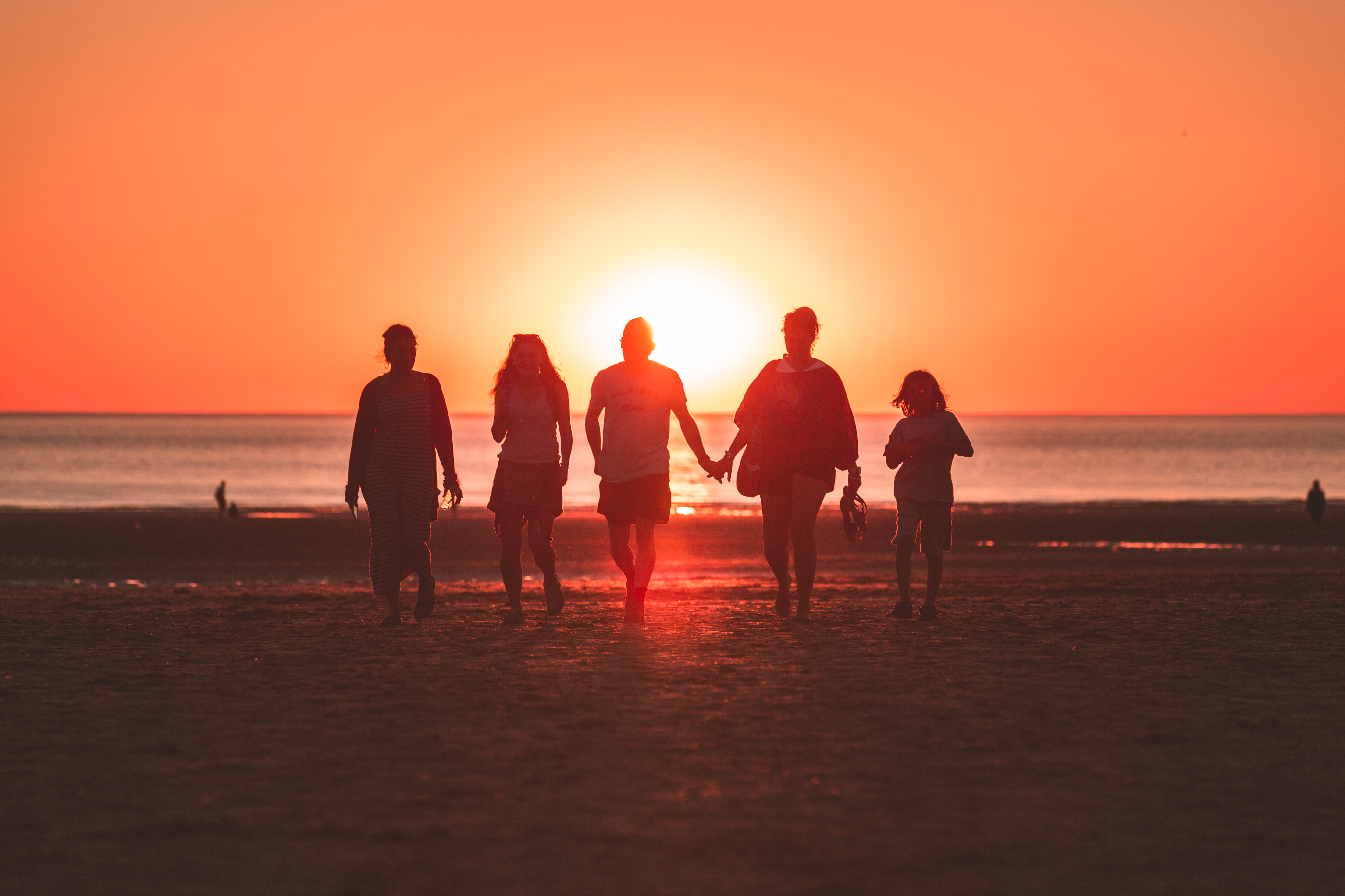 multi-generational travel family mebers walking along the beach at sunset